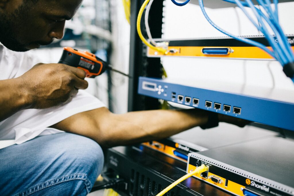 Side view crop concentrate African American male mechanic in jeans and white shirt using screw gun while working with hardware